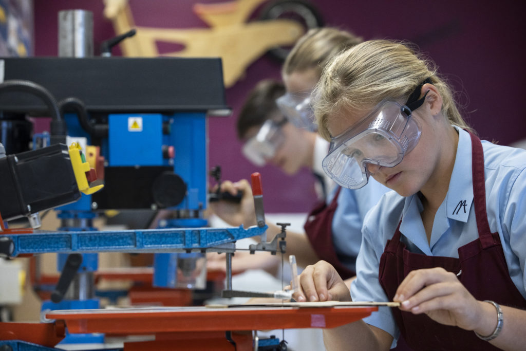 A female student can be seen wearing safety goggles, whilst using a machine during a Design & Technology class.